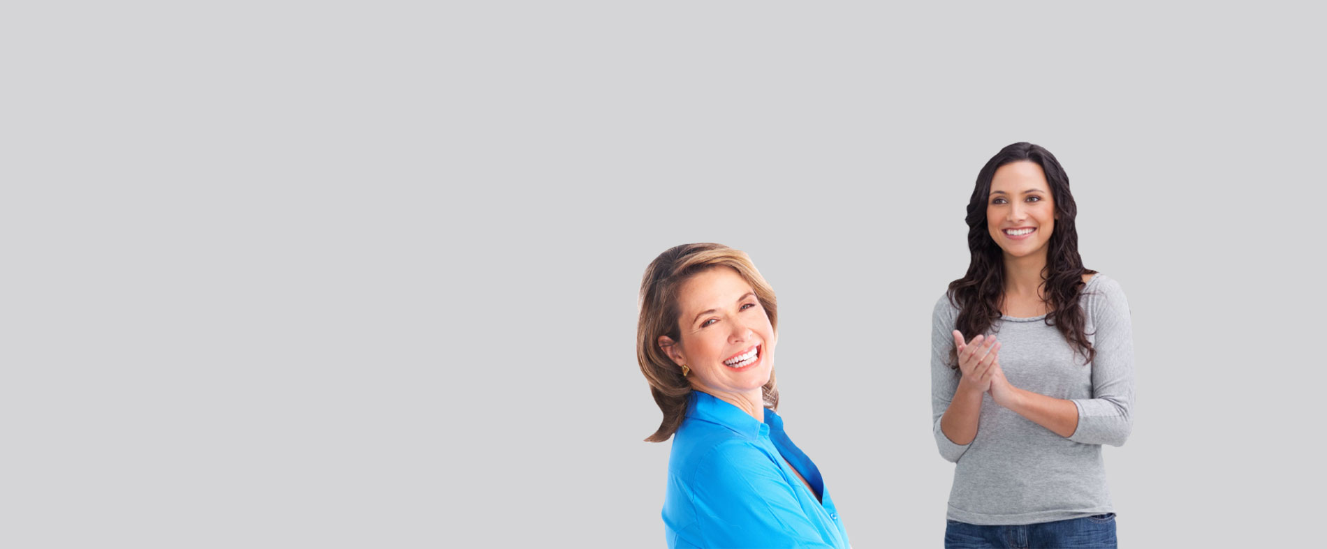 The image shows two individuals posing together with a backdrop one person appears to be a woman standing behind another person, who seems to be a man, both smiling and looking directly at the camera.